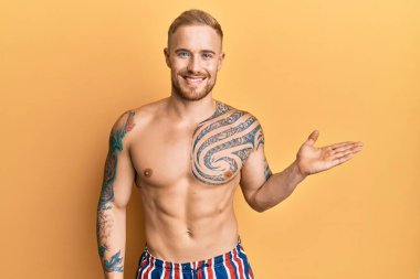 Mayo giyen genç, beyaz bir adam. Gülümseyen, neşeli bir gülümseme. Elleri avucunun içinde kameraya bakıyor.. 