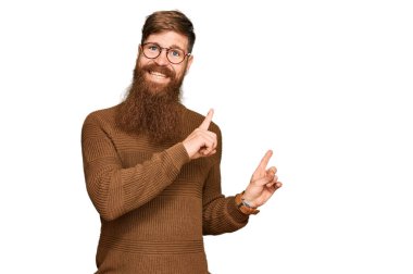 Genç İrlandalı kızıl elbiseli ve gözlüklü adam gülümseyip kameraya bakıyor ve iki eliyle ve parmaklarıyla kenarı işaret ediyor.. 