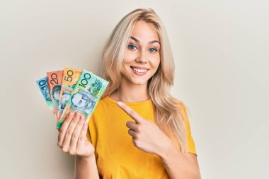 Güzel, beyaz, sarışın bir kız, elinde Avustralya doları, gülümsüyor, mutlu bir şekilde elini ve parmağını gösteriyor. 