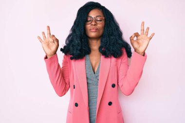 İş ceketi ve gözlük takan güzel Afrikalı kadın rahatla ve gülümse gözleri kapalı parmaklarıyla meditasyon hareketi yapıyor. yoga konsepti. 