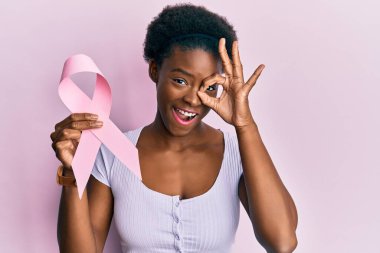 Genç Afro-Amerikalı kız pembe kanser kurdelesi tutuyor, gülümsüyor, mutlu mesut gülümsüyor. 