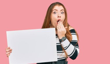 Genç, güzel, kızıl saçlı, elinde boş bir pankart tutan, ağzı eliyle kaplayan, şok olmuş ve hata yapmaktan korkan bir kadın. şaşırmış ifade 