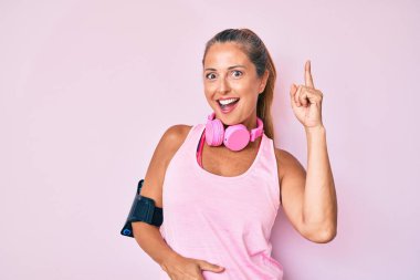 Orta yaşlı İspanyol kadın spor kıyafetleri giyiyor ve kulaklık takıp başarılı bir fikri işaret ediyor. Heyecanlı ve mutlu. Bir numara.. 