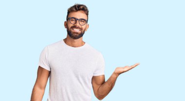 Gündelik kıyafetler ve gözlük takan genç İspanyol adam mutlu bir şekilde gülümsüyor ve avuç içi kameraya bakıyor.. 