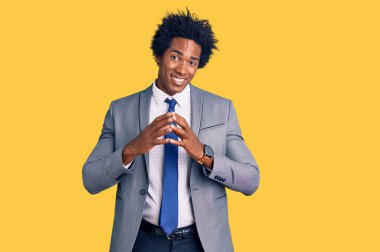 Afro saçlı, iş ceketi giyen ve gülümseyen, gevşemiş ve neşeli parmaklarını çapraz yapan yakışıklı Afro-Amerikalı adam. Başarı ve iyimserlik 