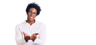 Afro saçlı, sıradan kıyafetler ve gözlük takan, elleri avuçlarında gülümseyen ve el hareketi yapan yakışıklı Afro-Amerikan bir adam. Bekleme ve koruma 