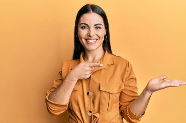 Genç esmer kadın, gündelik giysiler giyip kameraya hayret ediyor ve gülümsüyor.. 