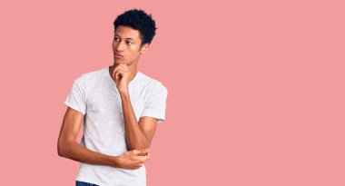 Beyaz bir tişört giyen genç Afro-Amerikalı adam ciddi bir yüz ifadesiyle eli çenesinde soruyu düşünüyor, kafa karıştırıcı bir fikir. 