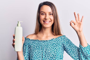 Genç, güzel bir kız elinde krem losyon şişesi tutuyor. Parmaklarıyla imza atıyor. Gülümsüyor. 
