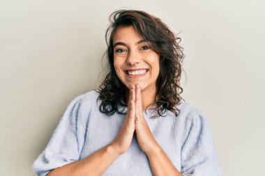 Gündelik bir kazak giyen genç İspanyol kadın elleriyle dua edip af diliyor kendinden emin bir şekilde gülümsüyor.. 