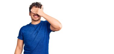 Kıvırcık saçlı, sıradan giyinen, gülümseyen ve yüzünde şaşkınlıktan gözleri kapayan genç, yakışıklı bir adam. kör kavram. 