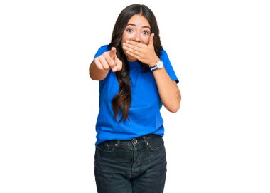 Güzel esmer, gündelik giysiler içinde genç bir kadın sana gülüyor, kamerayı işaret ediyor, ağzı kapalı, utanç ifadesi var. 