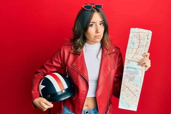 Young brunette woman holding motorcycle helmet and city map skeptic and nervous, frowning upset because of problem. negative person.