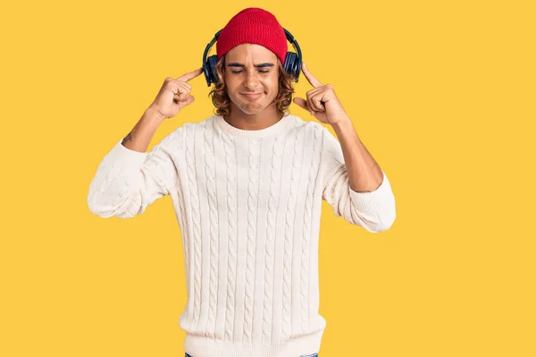 若いヒスパニック系の男は 大きな音楽のノイズのためのいらいらした表情で指で耳をカバーヘッドフォンを使用して音楽を聞いています 聴覚障害の概念 — ストック写真