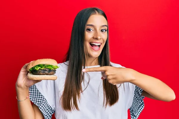 Fiatal Spanyol Hamburgert Eszik Mosolyogva Boldog Mutogatás Kézzel Ujjal — Stock Fotó