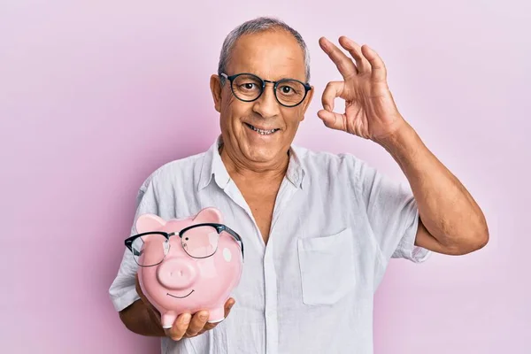 Pohledný Starší Muž Drží Prasátko Banky Brýlemi Dělá Znamení Prsty — Stock fotografie