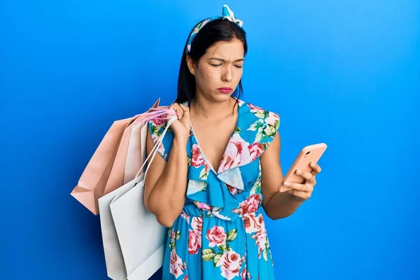 Jonge Latijnse Vrouw Met Winkeltassen Smartphone Sceptisch Nerveus Fronsen Boos — Stockfoto