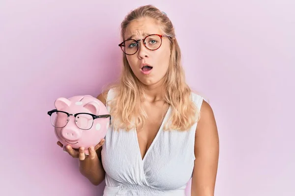 Jong Blond Meisje Holding Piggy Bank Met Bril Bang Verbaasd — Stockfoto