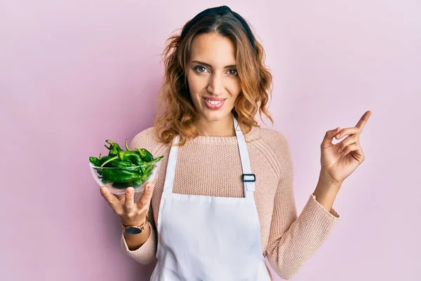 Ung Kaukasisk Kvinna Bär Förkläde Med Grön Paprika Skål Leende — Stockfoto