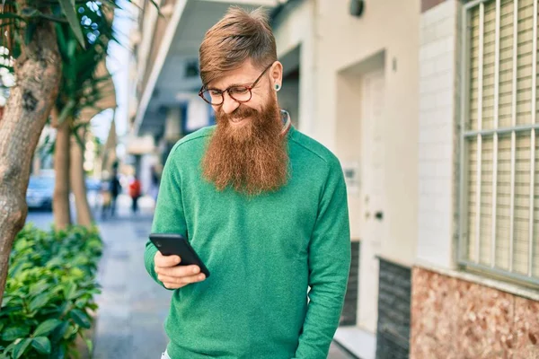 Young irish man with redhead beard smiling happy and using smartphone at the city.