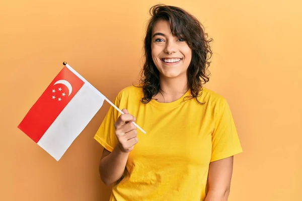 Молода Іспаномовна Жінка Тримає Сінгапурський Прапор Виглядає Позитивно Щасливо Стоячи — стокове фото