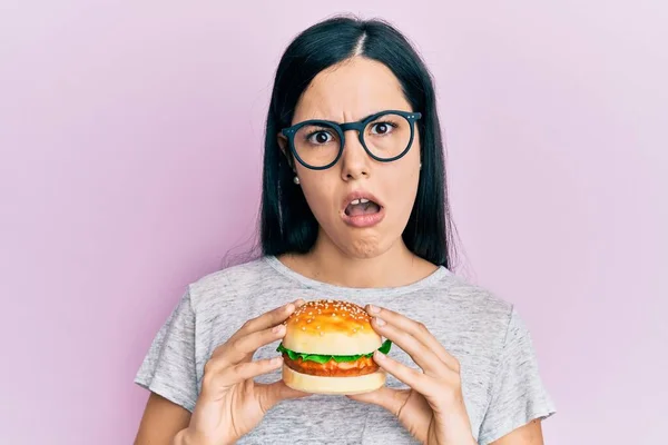Beautiful Young Woman Eating Tasty Hamburger Shock Face Looking Skeptical — Stock Photo, Image
