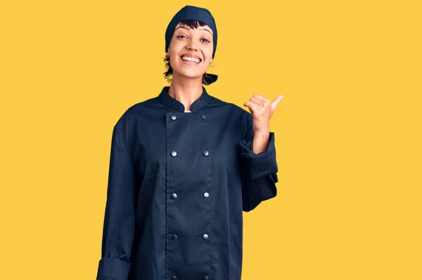 年轻的黑发女子 身穿职业厨师制服 面带微笑 面带微笑 大拇指指向旁边 — 图库照片
