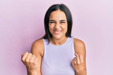 Genç esmer kadın gündelik giysiler giyiyor. Başarının şaşkınlığını ve şaşkınlığını kutluyor. Kolları havada ve gözleri kapalı. 