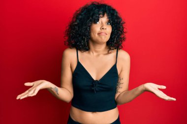 Kolsuz tişörtsüz, kolları ve elleri havada, kafası karışık bir ifade takınan İspanyol bir kadın. şüphe kavramı. 