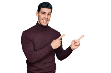 Yakışıklı, balıkçı yaka kazak giyen, gülümseyen ve kameraya bakan, iki eliyle ve parmaklarıyla yüzünü gösteren bir İspanyol.. 