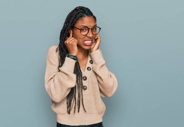 Gürültülü müzik sesi için kulaklarını parmaklarıyla kapatan sıradan kıyafetler giyen Afrikalı Amerikalı bir kadın. sağır kavramı. 