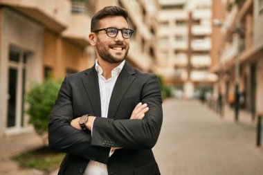 Kollarını kavuşturmuş genç İspanyol işadamı şehirde mutlu bir şekilde gülümsüyor..