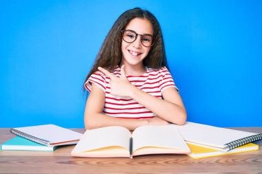 Tatlı İspanyol kız okul sınavına hazırlanıyor masaya oturmuş gülümsüyor, eli ve parmağı yan tarafta. 