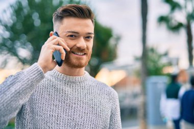Genç beyaz adam gülümsüyor. Şehirdeki akıllı telefondan konuşuyor..
