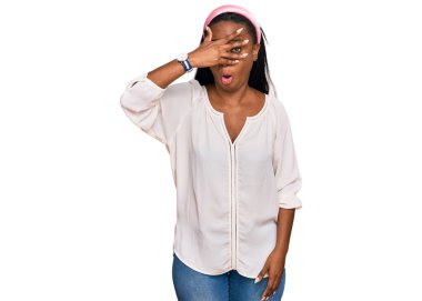 Gündelik kıyafetler giyen genç siyahi kadın şok içinde yüzünü ve gözlerini kapayarak utangaç ifadesiyle parmaklarının arasından bakıyor.. 