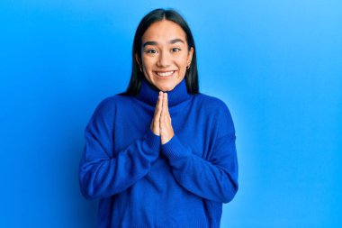 Sıradan bir kazak giyen genç Asyalı kadın ellerinin birarada dua ederek af diliyor kendinden emin bir şekilde gülümseyerek.. 