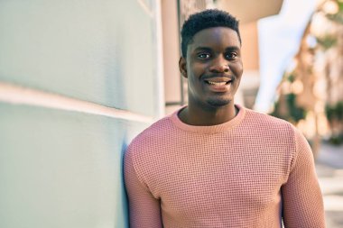Genç Afrikalı Amerikalı adam gülümseyerek şehirde mutlu mesut duruyor..