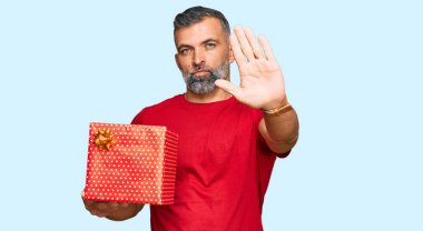 Orta yaşlı, yakışıklı, eli açık bir adam ciddi ve kendinden emin bir ifadeyle dur işareti yapıyor, savunma hareketi yapıyor. 