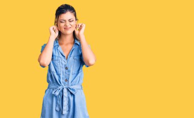 Gürültülü müzik sesi için kulaklarını parmaklarıyla kapatan sıradan kıyafetler giyen genç ve güzel bir kadın. sağır kavramı. 