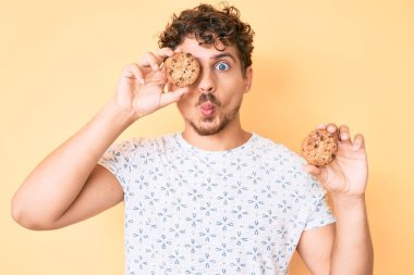 Kıvırcık saçlı, kurabiye tutan, ağzı balık suratlı, şaşı gözlü, çılgın ve komik bakışlı genç beyaz bir adam.. 