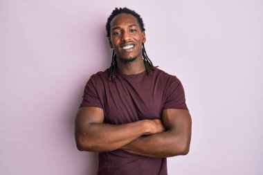 Saçları örgülü, mutlu yüzlü, kollarını kavuşturup kameraya bakan Afro-Amerikan bir adam. pozitif kişi. 