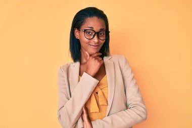 Genç Afro-Amerikan kadın iş kıyafetleri içinde kameraya bakarken kollarını kavuşturup gülümsüyor ve çenesini kaldırıyor. Olumlu düşünmek. 