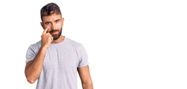 Gündelik giysiler giyen genç İspanyol adam senin jestini ve şüpheli ifadesini izleyerek gözüne işaret ediyor. 