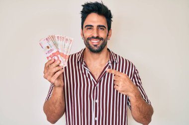 Sakallı, Kolombiya pezosu tutan yakışıklı İspanyol adam mutlu bir şekilde elini ve parmağını gösterdi. 