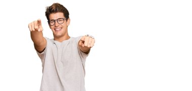 Yakışıklı beyaz adam, günlük kıyafetler ve gözlüklerle sana ve kameraya doğru bakıyor, pozitif ve neşeli gülümsüyor. 