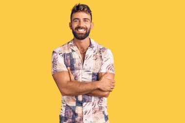 Yazlık kıyafetler giyen, kollarını kavuşturup kameraya gülümseyen genç İspanyol adam. pozitif kişi. 