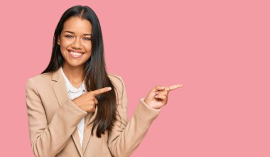 Güzel İspanyol kadın iş ceketi giyiyor gülümsüyor ve kameraya bakıyor iki eliyle ve parmaklarıyla kenarı işaret ediyor.. 