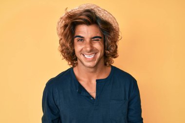 Yaz şapkası takan genç İspanyol adam kameraya seksi bir ifadeyle bakıyor, neşeli ve mutlu bir yüzle.. 