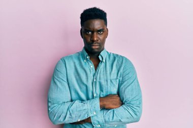 Yakışıklı, sıradan kıyafetler giyen, kuşkucu ve gergin, yüzünde çapraz kollu tasvip etmeyen siyahi bir adam. negatif kişi. 