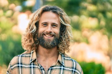 Parkta gülümseyen uzun saçlı beyaz bir genç..